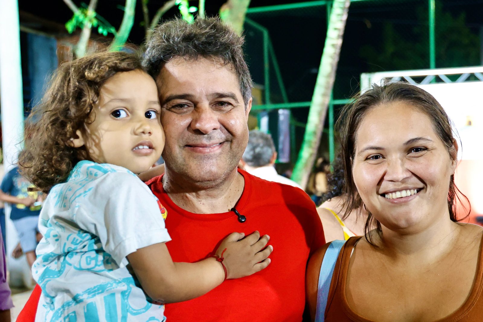 Prefeito Evandro posa para a foto com uma criança no braço e ao lado da mãe da menina